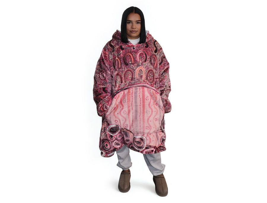 Woman wearing pink oversized hooded blanket with Indigenous aboriginal inspired artwork and plush fleece lining
