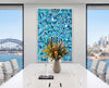 Bright contemporary interior featuring Listen Learn Teach, a large framed Aboriginal artwork in blue, turquoise, black, and white dot patterns displayed above a light wood cabinet beside tall sunlit windows