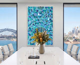 Bright contemporary interior featuring Listen Learn Teach, a large framed Aboriginal artwork in blue, turquoise, black, and white dot patterns displayed above a light wood cabinet beside tall sunlit windows